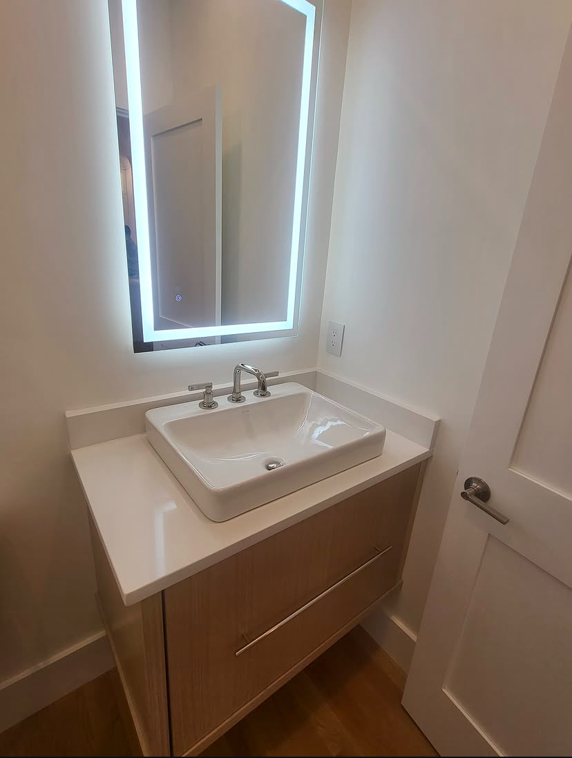 Powder room vessel sink on a floating wood vanity with a backlit LED mirror above it